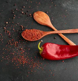 Ganze rote Chilischote und gemahlenes Chilipulver auf Holzlöffeln