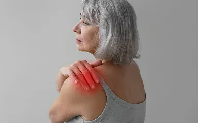 Frau im grauen Top, die eine Hand auf ihre Schulter legt