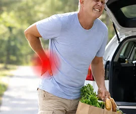 Mann mit einer Einkaufstasche, der sich mit der Hand an den unteren Rücken fasst